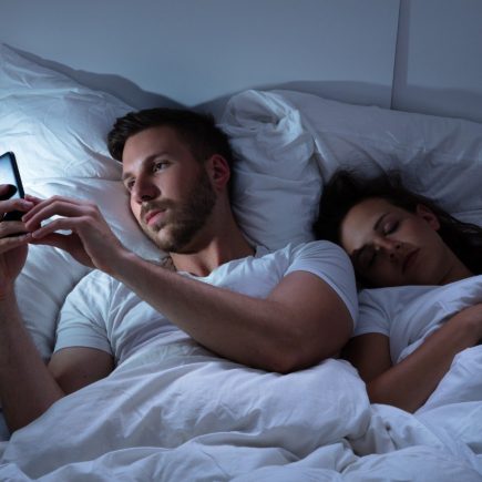 man looking at his phone while his partner is sleeping