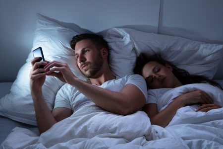 man looking at his phone while his partner is sleeping